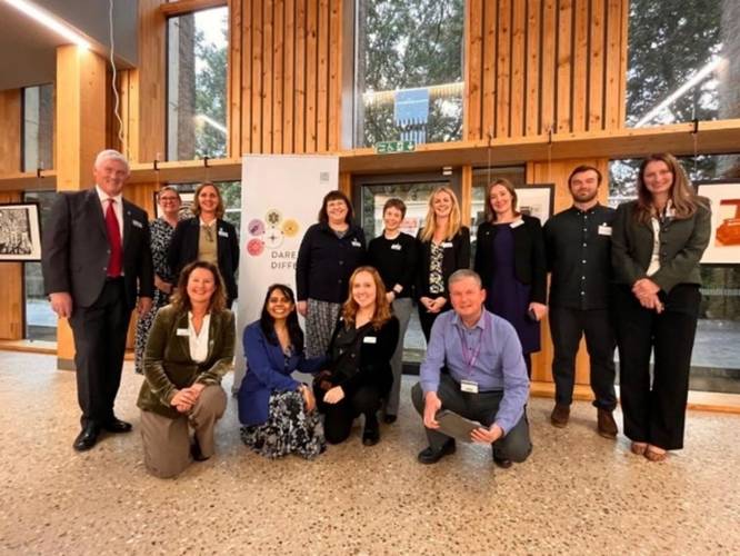 The Development, Alumni, and Campaigns team at UEA Court, standing and kneeling in front of a 'Dare to Do Different' campaign banner, celebrating the launch of the new fundraising initiative.
